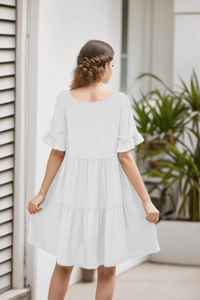 Rear view of white tiered babydoll dress with ruffle sleeves and three-layer pleated hem