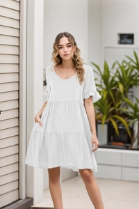 Detail of V-neck white tiered dress with ruffle sleeves and airy pleated fabric texture