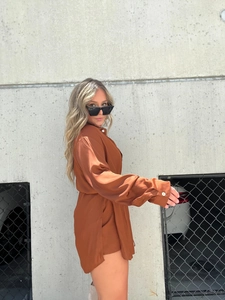 Detail of rusty orange satin long sleeve bodysuit with elegant pearl button cuffs