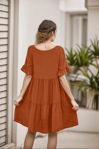 Detail of rust red baby doll dress featuring three-tier pleated skirt and ruffled sleeves