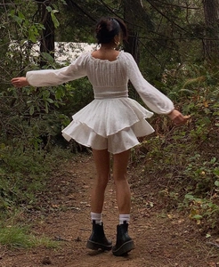 Detail of white cottagecore dress featuring tiered skirt and puff sleeves in forest