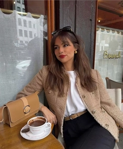 Close-up of a tweed jacket with metal buttons and a leather handbag in a cafe setting