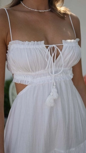 Detail of white bohemian maxi dress with delicate ruffles, tassels, and side cut-outs