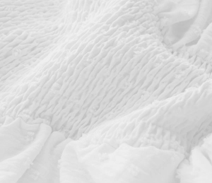 Detailed close-up of white smocked fabric featuring elegant Swiss dots texture for jumpsuit