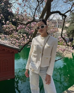 Detail of cream tweed jacket with gold buttons and white quilted chain bag in spring garden
