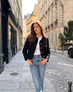 Detail of a black tweed jacket with gold buttons paired with blue jeans in a street setting
