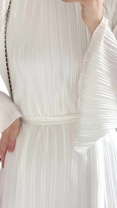 Detail of white micro-pleated dress showing trumpet sleeves and high-waisted tie closure