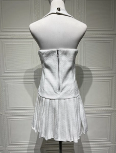 Nahaufnahme von weißem Tweed-Gewebe, goldenem Knopf und Reißverschluss am Plisseekleid