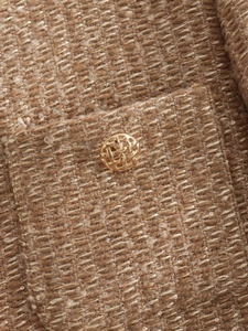 Close-up of golden textured metal button on sequined brown tweed jacket fabric