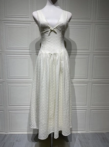 Dettaglio dell'abito bianco con scollo a V, ricamo traforato e fiocco decorativo