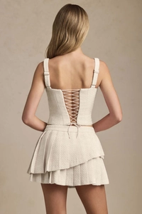 Detail of the cream tweed two-piece set featuring back cross-lace straps and pleated skirt