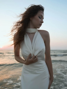 Detail of elegant white satin halter neck dress against a beach sunset backdrop