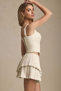 Detail of cream tweed two-piece set featuring lace-up back top and pleated mini skirt