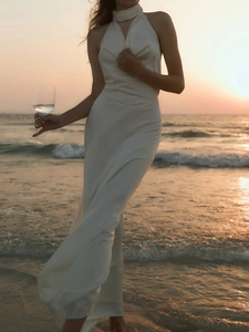 Elegantly draped ivory satin halter maxi dress with an open back at sunset beach