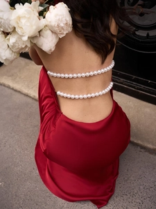 Detail view of red satin backless dress featuring elegant double pearl chain draping