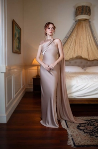 Detail of elegant champagne satin dress featuring one-shoulder design and flowing cape