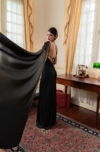 Detail of elegant black satin backless evening gown with long cape and tie-up back