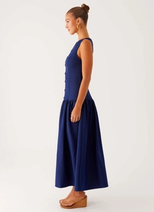 Side view of long sleeveless navy denim dress with button-down front and flared skirt hem