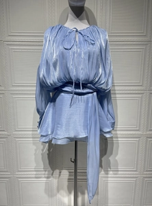 Detail of light blue pleated glossy fabric set featuring a tie neck and ruffled hemline