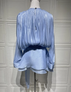 Detail of light blue glitter pleated blouse featuring vertical folds and shimmering fabric