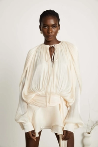 Detail of elegant beige puff sleeve blouse featuring shimmer pleated fabric and tie-up neck