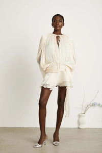 Detailed view of cream pleated dress featuring layered ruffle hem and puff sleeves