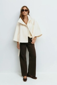 Detail view of high-neck ivory cape coat with batwing sleeves and button accents