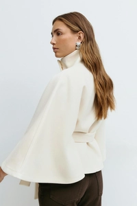 Detail view of the beige wool-like poncho coat featuring a high collar and cinched waist belt