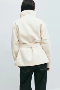 Detail view of cream wool coat back showing standing collar and waist belt detail