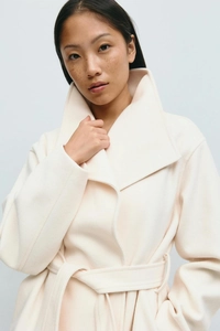 Detailed view of the thick wool blend texture and waist belt on a cream winter coat