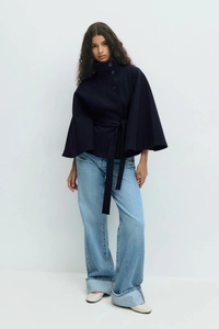 Detail of high neck dark blue cape coat with buttons and belt on a studio model