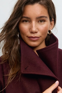 Detailed close-up of burgundy high-neck wool coat fabric and collar stitching details