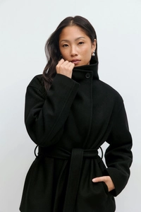 Detail of a black wool coat featuring a wrap belt design and elegant single collar button