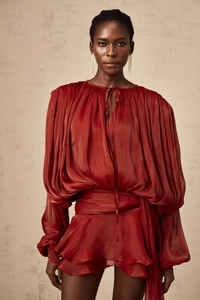 Detail of deep red pleated fabric with V-neck tie and elegant billowing sleeves