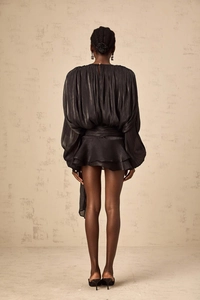 Detail showing back pleats and tiered ruffle hem of a shiny black French style mini dress