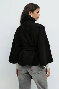 Back view of a black cape-style coat with belt and wool texture on studio background