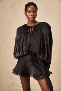 Detail of black pleated fabric dress featuring lantern sleeves and wavy hem design