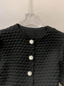 Detail of white pearl gold buttons on a black textured honeycomb knit blouse
