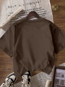 Détail d'un t-shirt col rond marron foncé en coton épais posé sur un sol rustique