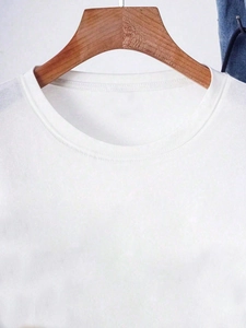 Close-up of the crew neck and shoulder detail on a white cotton T-shirt hanging on a wooden hanger