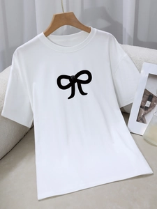 White crew neck T-shirt with black bow print and 3D bead detail on a wooden hanger