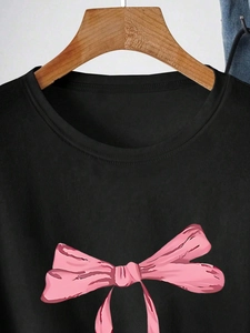 Detail of a black crew neck T-shirt featuring a pink ribbon bow graphic on wooden hanger