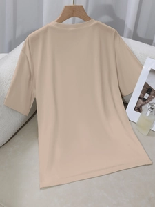 Beige T-shirt met korte mouwen en ronde hals aan een houten hanger in een sfeervol interieur