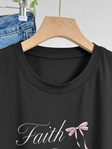 Détail de l'imprimé Faith et du nœud rose sur le t-shirt noir en coton à col rond