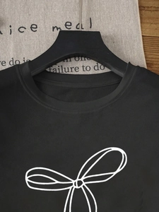 Dettaglio di una t-shirt nera a girocollo con stampa a fiocco bianco minimalista sul petto