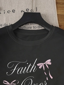 Détail de l'imprimé Faith et du nœud rose sur le t-shirt noir en coton à col rond