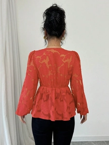 Detail of orange floral textured blouse featuring puff sleeves and peplum waist design