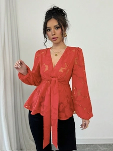 Detail of red V-neck blouse featuring semi-transparent floral jacquard and waist tie-belt