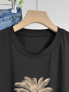 Minimalist black crew neck cotton T-shirt with palm leaf print on a wooden hanger