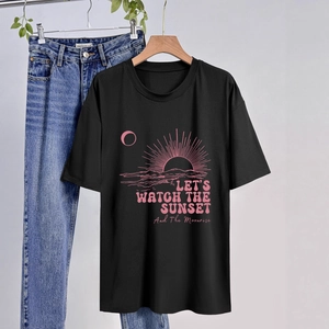 Dettaglio di una maglietta nera con grafica tramonto rosa e scritta decorativa
